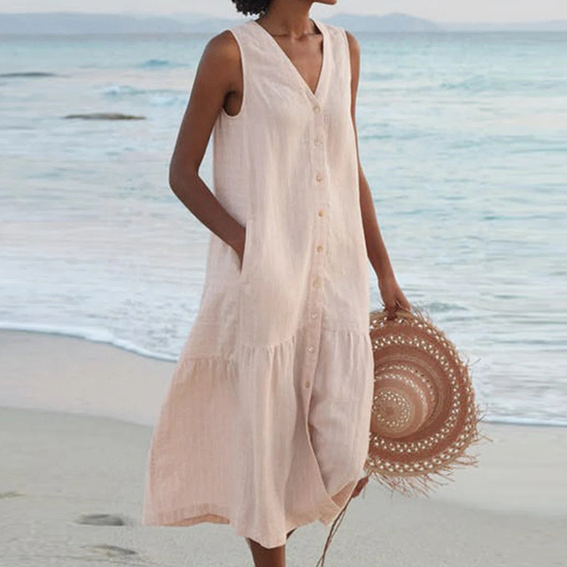 Robe d'été beige sans manches sur une femme à la plage, tenant un chapeau en paille. Mode estivale, tenue décontractée bord de mer.