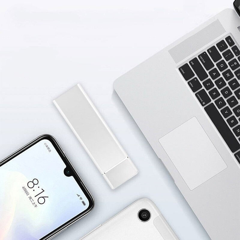 Ordinateur portable argenté avec smartphone et clé USB blanche sur un bureau blanc. Accessoires technologiques modernes, design épuré.
