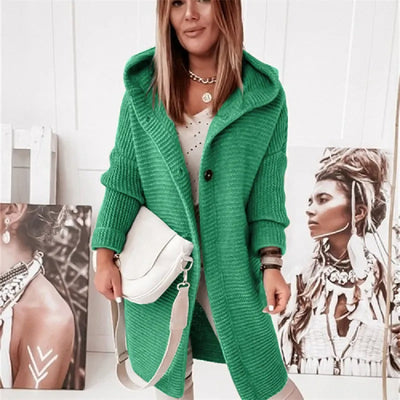 Femme portant un manteau vert en tricot avec capuche, posant devant des portraits artistiques. Mode automne, style décontracté, accessoires tendance.