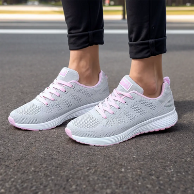 Chaussures de course grises et roses pour femmes sur trottoir, design respirant, semelle antidérapante, idéales pour jogging et fitness.