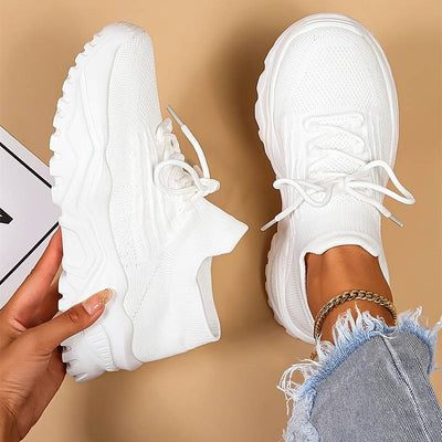 Chaussures de sport blanches modernes sur fond beige, portées avec un jean déchiré. Sneakers tendance, confortables et élégantes pour un look décontracté.
