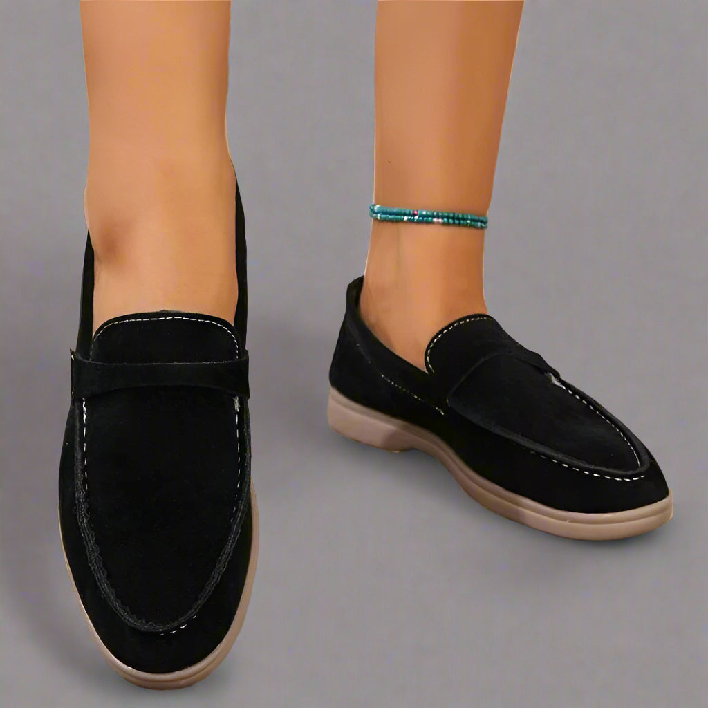 Chaussures mocassins noirs en daim pour femme, semelle beige, portées avec un bracelet de cheville turquoise. Mode élégante et confortable.
