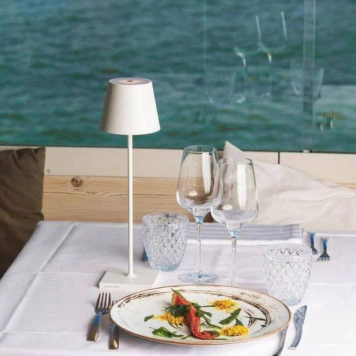 Assiette gastronomique avec poisson et légumes sur table élégante, vue sur mer, verres à vin, lampe moderne, restaurant bord de mer.