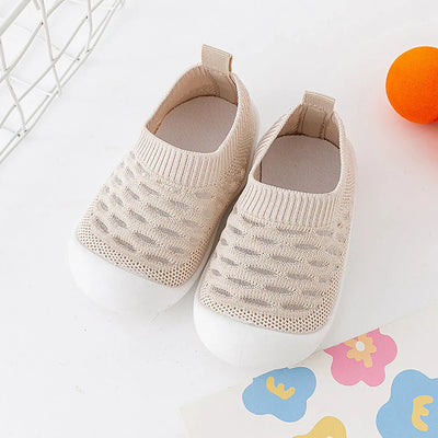 Chaussures bébé en tricot beige avec semelle blanche, posées sur fond blanc. Accessoires colorés à proximité. Confortables et élégantes pour enfants.