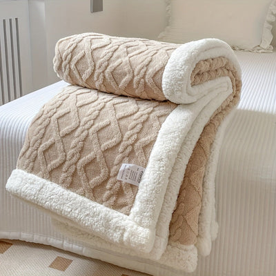 Couverture en laine beige et blanche à motifs géométriques, posée sur un lit blanc. Décoration intérieure, confort, literie élégante.