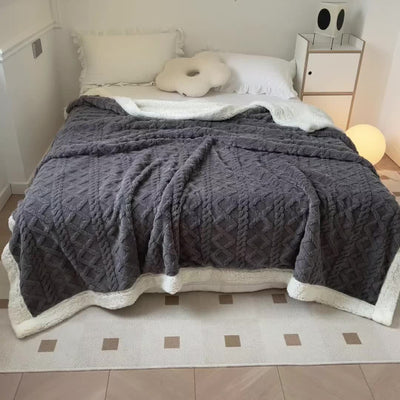 Lit moderne avec couverture grise texturée, coussin décoratif blanc, et table de chevet minimaliste. Chambre élégante et confortable.