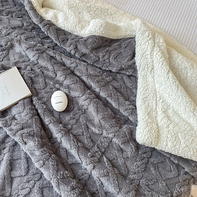 Couverture en polaire grise et blanche sur un lit, avec un livre et un œuf de bain Chanel. Literie confortable, accessoires de luxe, détente.