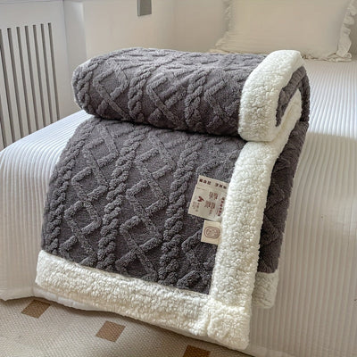 Couverture en laine grise texturée avec bordure blanche en peluche, posée sur un lit blanc. Design élégant et confortable pour chambre moderne.