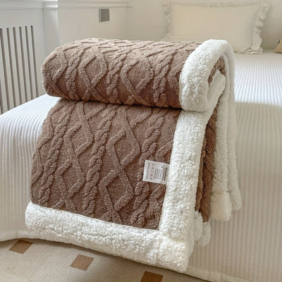Couverture en laine marron avec motif géométrique et bordure blanche en peluche, posée sur un lit blanc. Accessoire de chambre cosy et élégant.