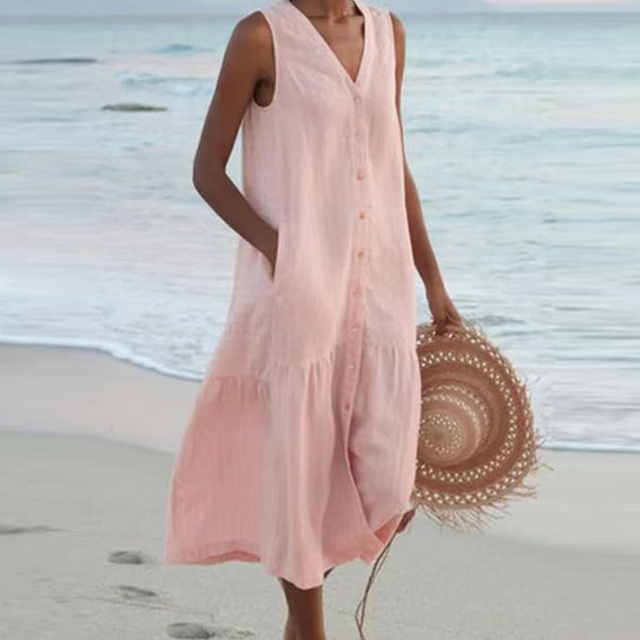 Robe d'été rose sans manches sur femme à la plage, tenant un chapeau en paille. Mode estivale, tenue décontractée bord de mer.