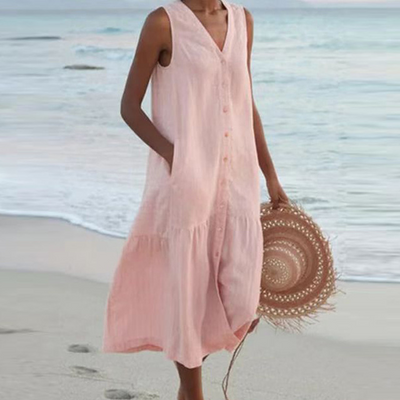 Robe d'été rose sans manches sur femme à la plage, tenant un chapeau en paille. Mode estivale, tenue décontractée bord de mer.
