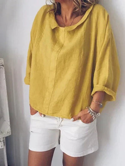 Femme portant une blouse jaune en lin avec manches retroussées et short blanc. Mode estivale décontractée, tenue élégante et confortable.