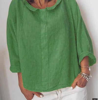 Femme portant une blouse verte en lin avec manches retroussées, associée à un pantalon blanc. Mode décontractée, style estival, tenue élégante.