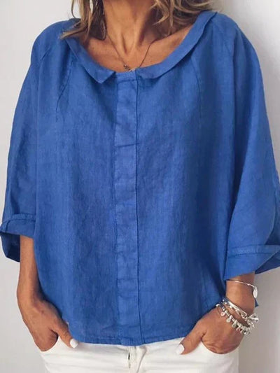 Blouse en lin bleu pour femme, manches trois-quarts, col rond, portée avec un pantalon blanc. Mode féminine élégante et décontractée.