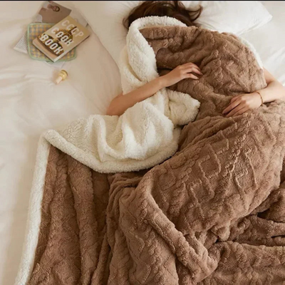 Personne dormant sous une couverture en fausse fourrure marron et blanche sur un lit, avec des livres et une tasse de café à proximité.
