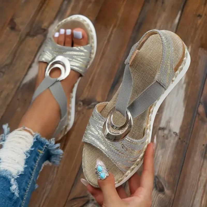 Sandales compensées grises élégantes avec détails métalliques circulaires, portées avec un jean déchiré. Mode estivale, chaussures tendance femme.