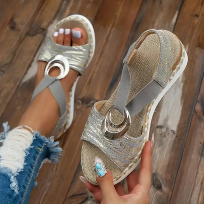 Sandales compensées grises élégantes avec détails métalliques circulaires, portées avec un jean déchiré. Mode estivale, chaussures tendance femme.
