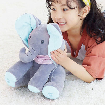 Jeune fille souriante avec un éléphant en peluche gris et bleu, allongée sur un tapis blanc. Jouet doux, enfant heureux, moment de jeu.
