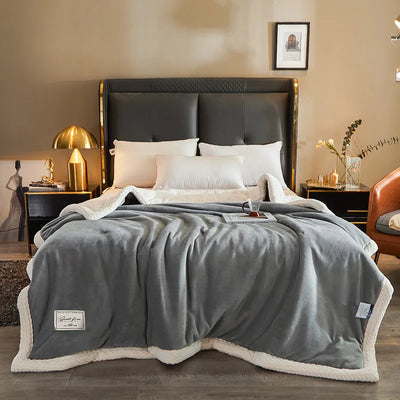 Lit moderne avec couverture en polaire grise, oreillers blancs, lampe dorée et décoration élégante. Chambre contemporaine et confortable.