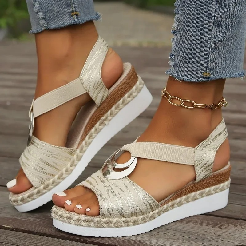 Sandales compensées beiges pour femme avec semelle en corde, ornées de détails métalliques, portées avec un jean déchiré et bracelet doré.