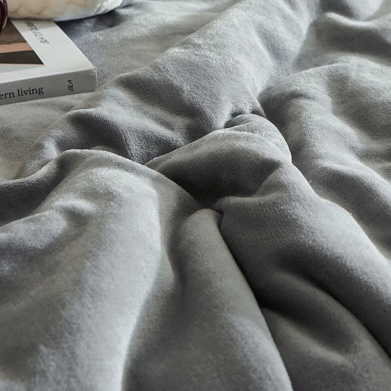 Couverture en polaire grise douce sur un lit, avec un livre sur le design d'intérieur moderne à côté. Confort, chaleur, décoration chambre.