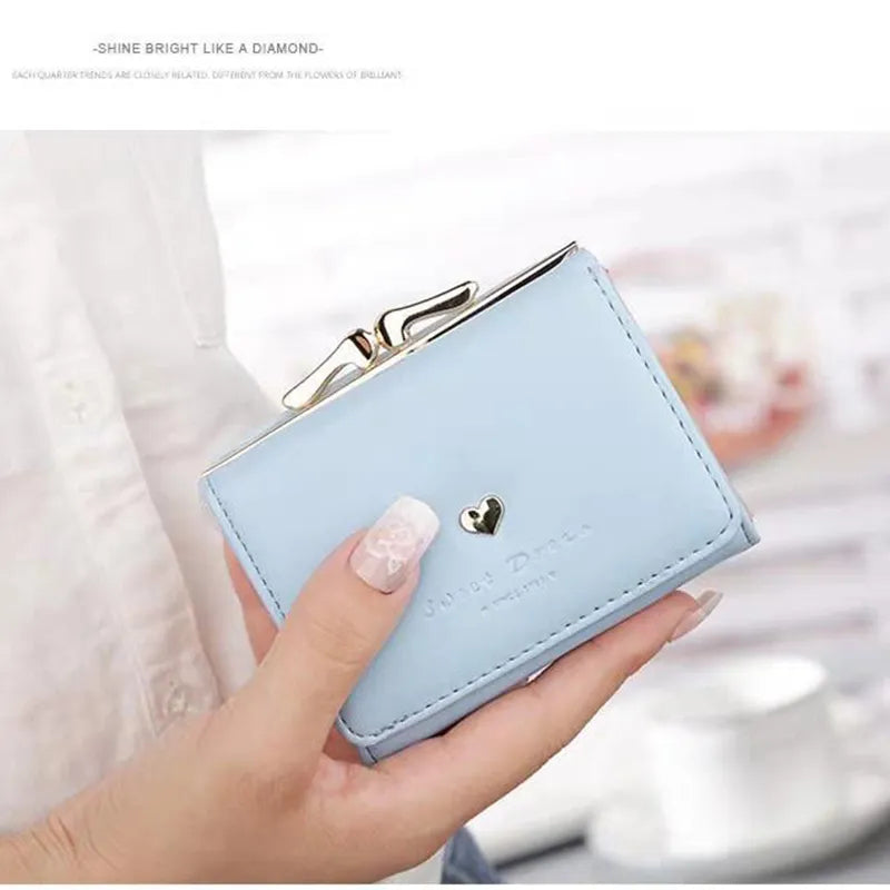 Portefeuille bleu en cuir avec fermoir doré et cœur décoratif, tenu par une main avec manucure élégante. Accessoire mode chic et tendance.