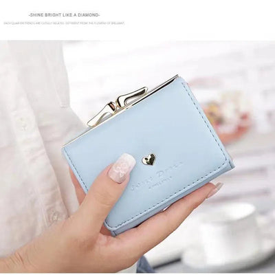 Portefeuille bleu en cuir avec fermoir doré et cœur décoratif, tenu par une main avec manucure élégante. Accessoire mode chic et tendance.
