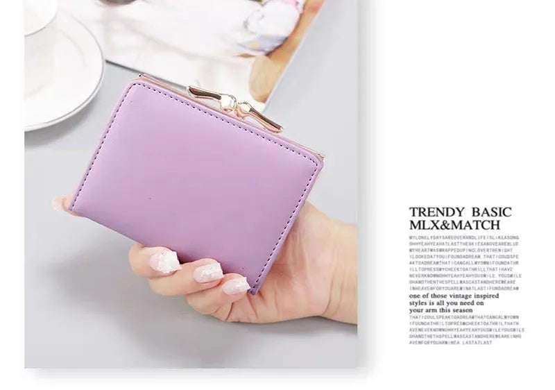 Portefeuille violet en cuir synthétique, tenu par une main avec des ongles manucurés, posé sur une table blanche avec une tasse en arrière-plan.