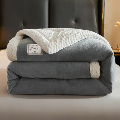 Couverture en polaire grise et blanche, pliée sur un lit, avec motif chevron et étiquette visible. Literie douce et confortable pour chambre moderne.