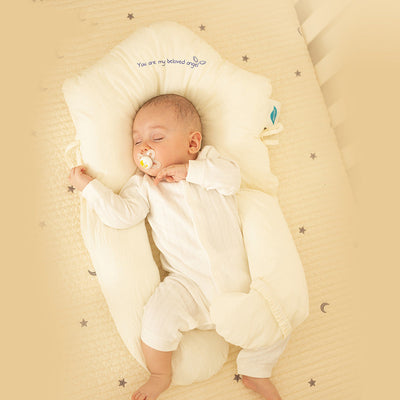 Bébé endormi dans un lit bébé, vêtu de blanc, avec une tétine. Coussin de soutien beige, décor étoilé. Confort et sécurité pour nouveau-né.
