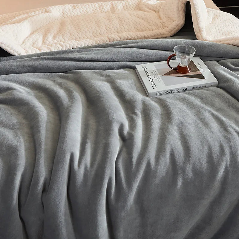 Couverture en laine grise sur un lit, avec une tasse en verre et un livre. Literie confortable, décoration intérieure moderne, chambre cosy.