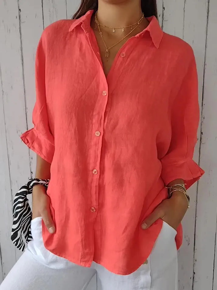 Chemise en lin corail pour femme, manches retroussées, col classique, portée avec un pantalon blanc. Mode estivale élégante et décontractée.