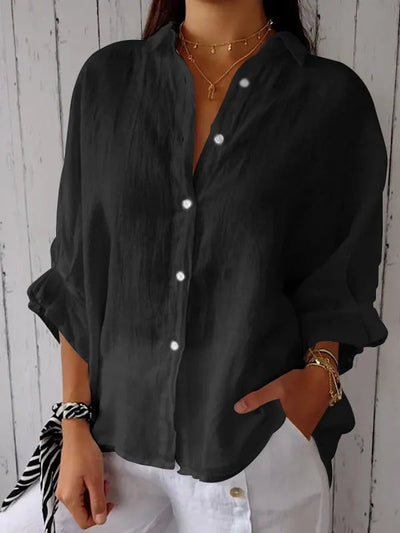 Chemise noire en lin pour femme, manches longues retroussées, boutons blancs, portée avec un pantalon blanc. Style décontracté et élégant.