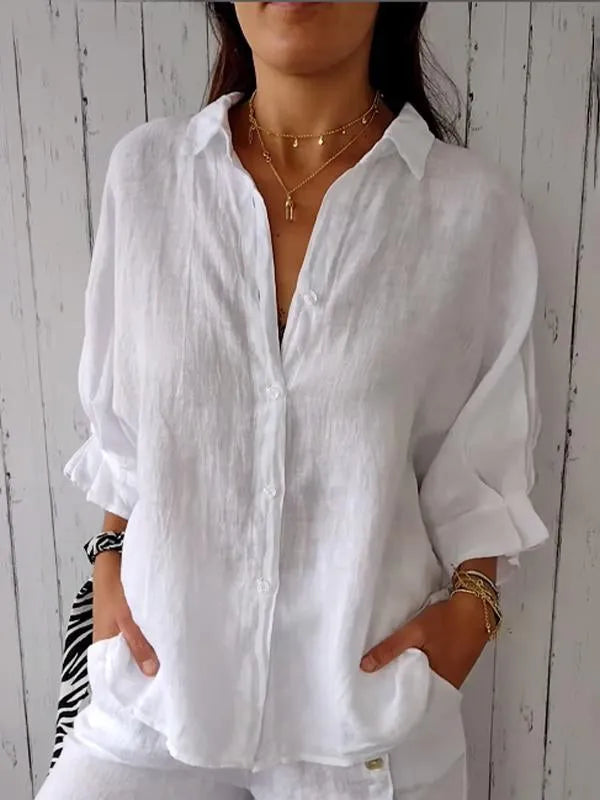 Chemise en lin blanc pour femme, manches retroussées, col ouvert, portée avec colliers dorés. Mode décontractée, élégance estivale.
