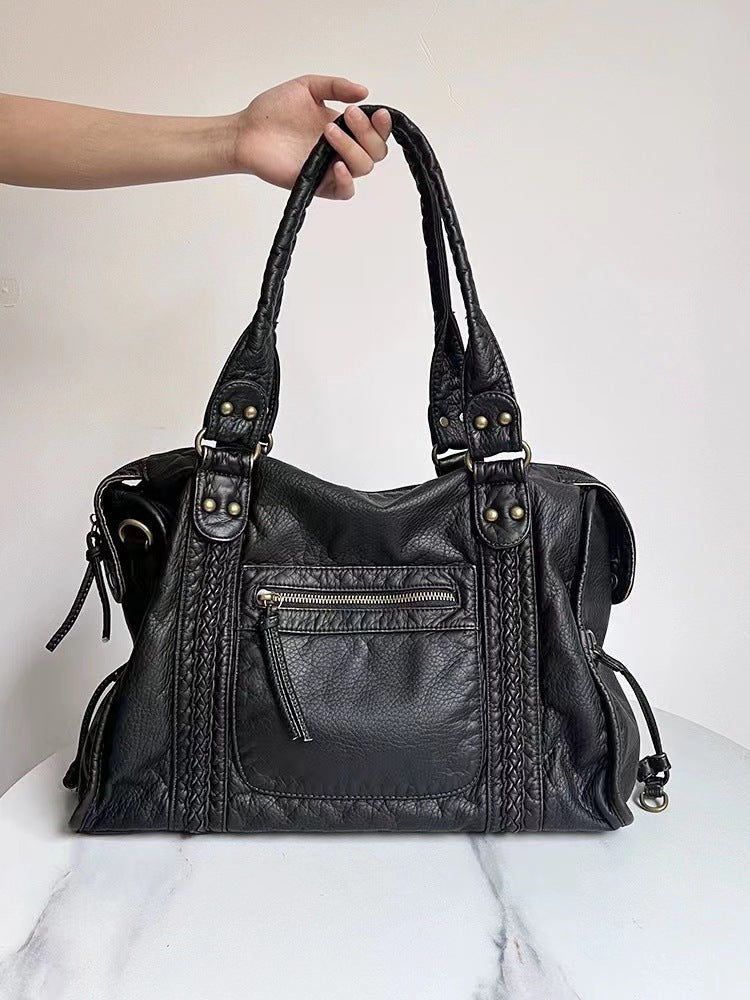 Sac à main en cuir noir avec poignées tressées, poche zippée avant, détails métalliques dorés. Accessoire mode élégant et tendance.