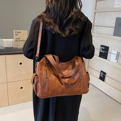 Femme de dos portant un sac à main en cuir marron avec bandoulière, dans un intérieur moderne. Mode, accessoires, sac tendance, style urbain.