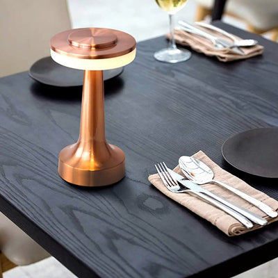 Lampe de table en cuivre moderne sur une table en bois sombre, entourée de couverts élégants et de verres à vin, créant une ambiance chic et sophistiquée.
