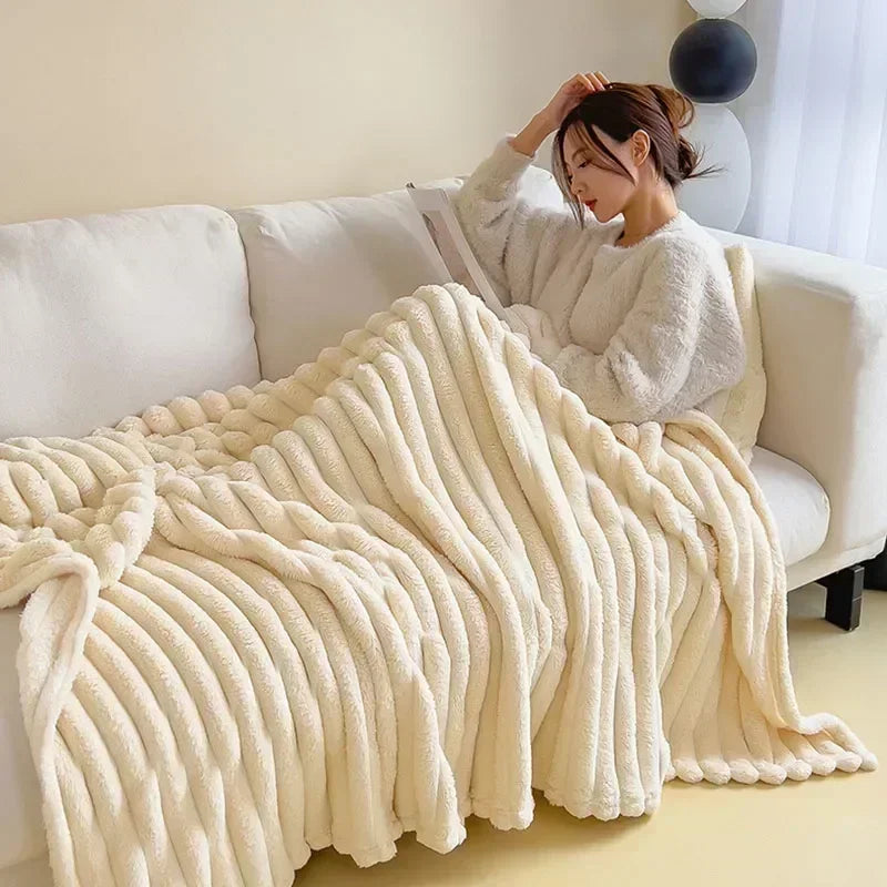 Femme lisant sur un canapé, enveloppée dans une couverture en fausse fourrure beige. Ambiance cosy, détente à la maison, décoration intérieure moderne.