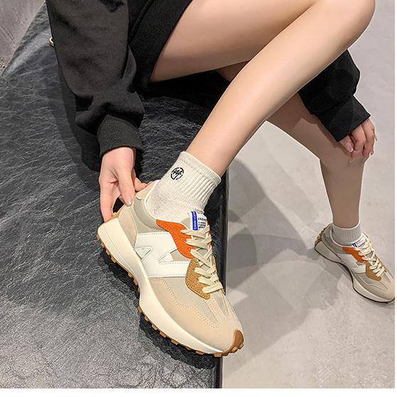 Baskets beige et orange sur un banc noir, portées avec des chaussettes blanches. Mode urbaine, chaussures tendance, style décontracté.