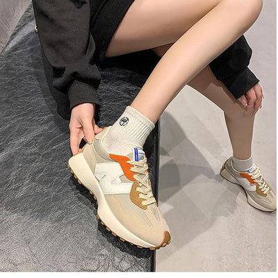 Baskets beige et orange sur un banc noir, portées avec des chaussettes blanches. Mode urbaine, chaussures tendance, style décontracté.