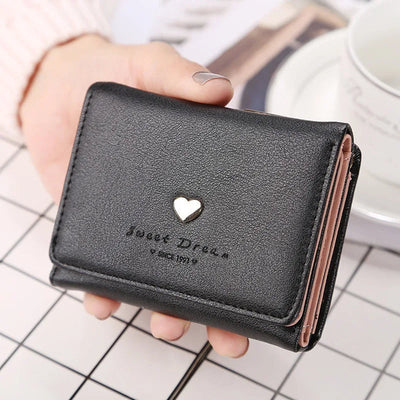 Portefeuille en cuir noir avec un motif de cœur doré, tenu par une main. Accessoire élégant pour femmes, idéal pour organiser cartes et billets.