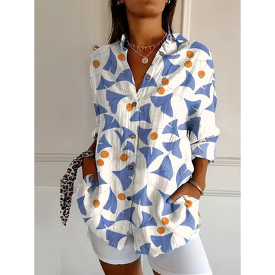 Chemise femme à motifs floraux bleus et oranges, manches longues, col classique, boutons en bois, portée avec un short blanc. Mode tendance.