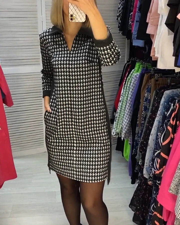 Robe pied-de-poule noir et blanc, manches longues, portée par une femme dans une cabine d'essayage, entourée de vêtements colorés.