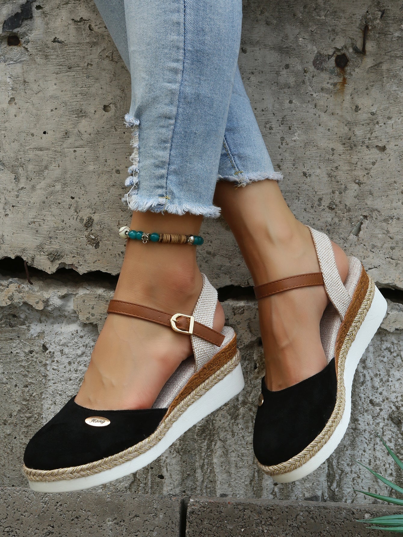 Sandales compensées noires en daim avec bride marron, portées avec un jean déchiré. Chaussures d'été tendance pour femmes, style décontracté.