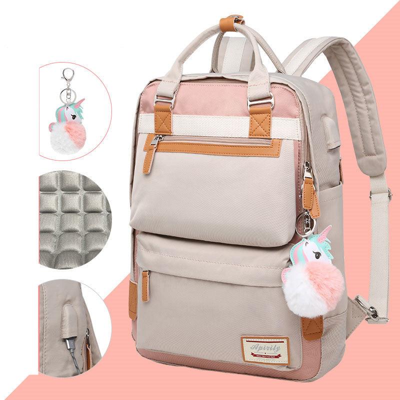 Sac à dos beige et rose avec porte-clés licorne, poches multiples, détails en cuir marron, fermeture éclair robuste. Accessoire mode tendance.