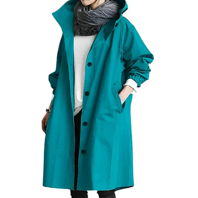 Manteau long turquoise avec capuche, porté par une personne, sur fond blanc. Mode automne-hiver, style décontracté, tendance féminine.