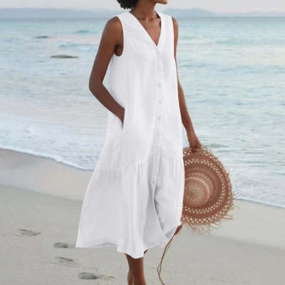 Robe blanche sans manches, femme tenant un chapeau de paille, marchant sur une plage au bord de la mer. Mode estivale, tenue décontractée plage.