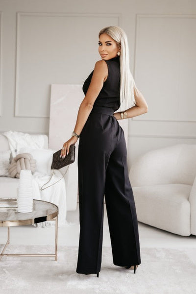 Femme élégante en combinaison noire, tenant un sac à main, posant dans un salon moderne. Mode chic, style sophistiqué, décoration intérieure.