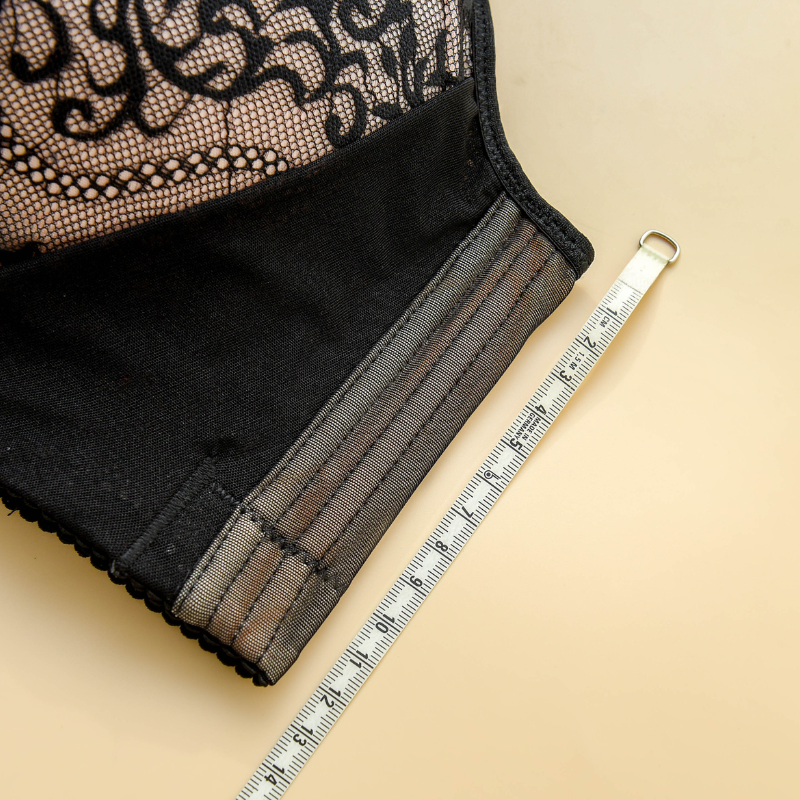 Corset noir en dentelle avec fermeture à crochets, mesuré par un ruban à mesurer blanc sur fond beige. Mode féminine, lingerie élégante.