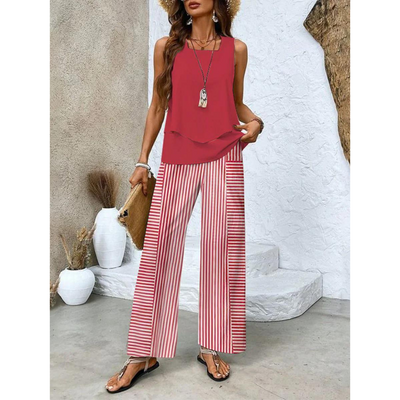 Femme en tenue estivale chic, portant un haut rouge et un pantalon rayé rouge et blanc, accessoirisée d'un chapeau de paille et d'un sac en osier.